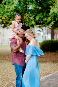 Dad holds child on shoulders while posing with mom for spring family photograph.