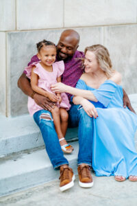 Family sits on steps of macon colosseum together in colorful outfits for spring family photography